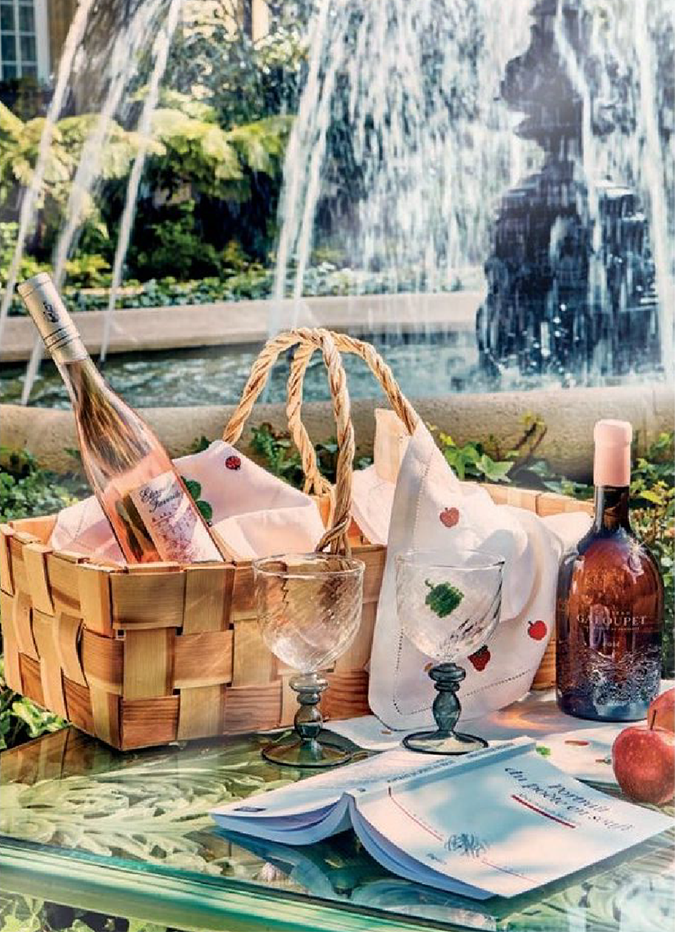 Panier en osier avec bouteille de rosé, verre et serviette près d'une fontaine, tableaux et accessoires de table